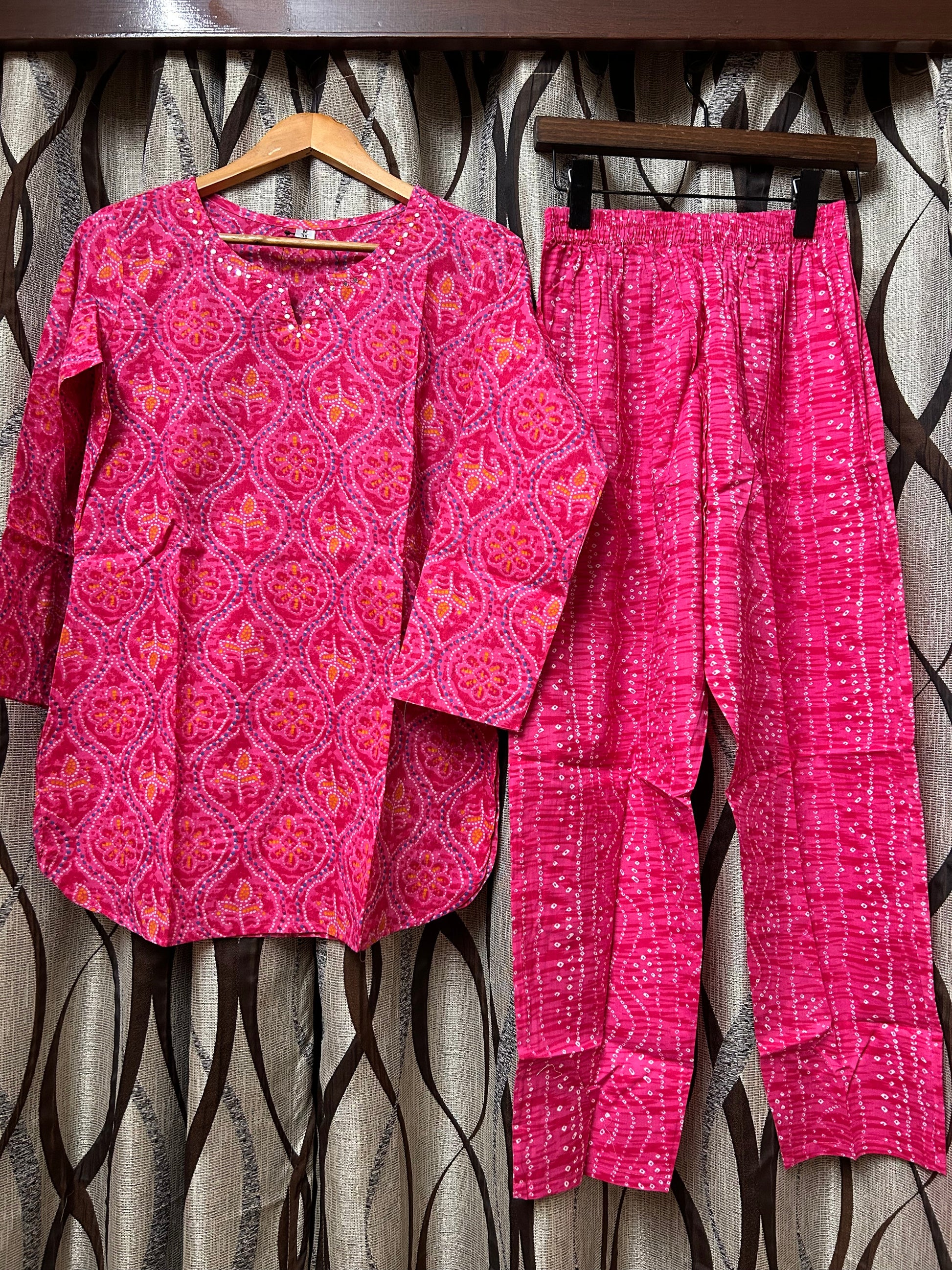 Rani pink bandhani kurti and pants on hangers against dark background