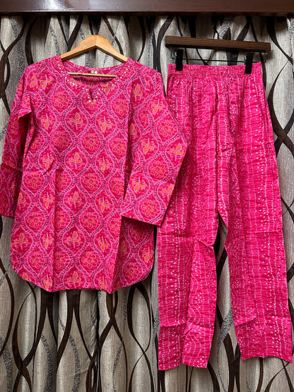 Rani pink bandhani kurti and pants on hangers against dark background