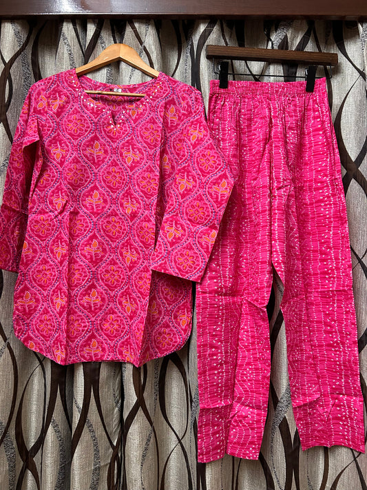 Rani pink bandhani kurti and pants on hangers against dark background